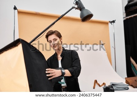stunning joyous woman with photography equipment smiling cheerfully at camera in her studio