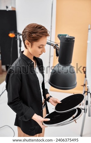 young pretty brunette woman with short hair looking at her photography equipment in her studio