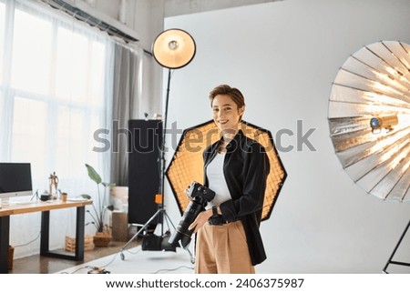 cheerful pretty woman with short hair in everyday clothes posing in her studio with camera in hands