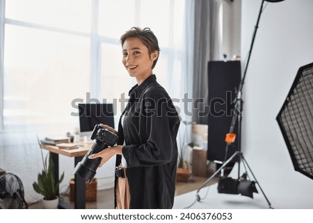 happy young female photographer with short hair posing with her camera and smiling cheerfully