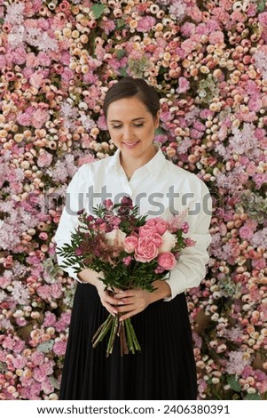 Stylish happy brunette woman with cute smile holding flower gift and posing on pink floral background.  Blooming, love, 8 march birthday holiday concept