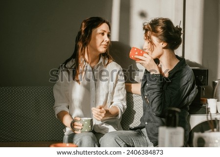 Two female friends enjoying morning coffee in a cozy home kitchen Sunny morning and friendly conversations between two young women Royalty-Free Stock Photo #2406384873