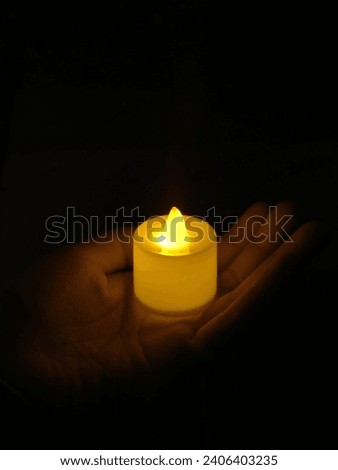 Warm white candlelight light held on hands on a dark background.