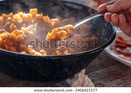 Cooking the typical Spanish dish of "Migas Castellanas" over a wood fire and you can see the entire process along with its ingredients such as bread, chistorra, peppers, garlic, bacon, grapes  Royalty-Free Stock Photo #2406421577