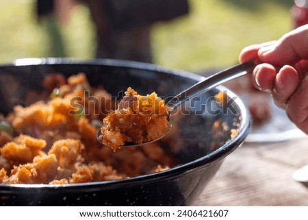 Cooking the typical Spanish dish of "Migas Castellanas" over a wood fire and you can see the entire process along with its ingredients such as bread, chistorra, peppers, garlic, bacon, grapes  Royalty-Free Stock Photo #2406421607