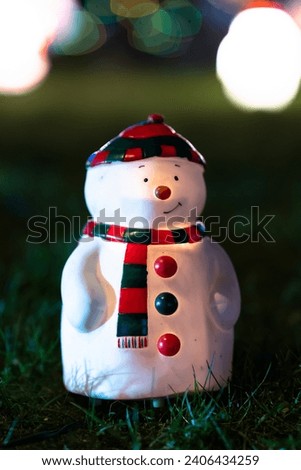 The picture of a little christmas decoration - a smiling snowman on the geen grass. Snowman glowing from inside. Very funny toy. Vertical high resolution photo.