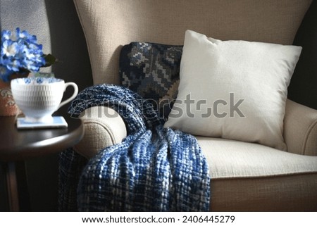 Plain canvas throw pillow suitable for mock up mockup on a chair with blue throw blanket - your design, message or logo Royalty-Free Stock Photo #2406445279