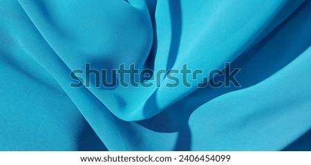 Wavy turquoise cyan translucent fabric in the sun, in folds (macro, blue crepe chiffon, texture). Royalty-Free Stock Photo #2406454099