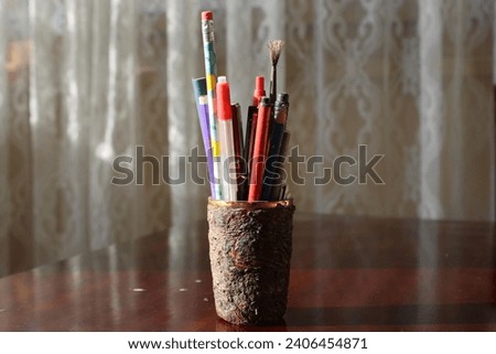 An image that captures a handmade mug with a bunch of pens and pencils on a table.