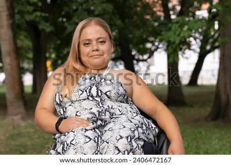 Smiling Brightly Young Woman With Short Stature Sitting In Wheel Chair In Green Park Outdoor. October Dwarfism Awareness Month. Horizontal. High quality photo Royalty-Free Stock Photo #2406472167