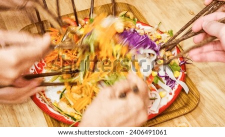 People mixing and tossing Japenese recipe yusheng or yee sang with salmon sashimi during Chinese New Year dinner celebration. Slow shutter speed with motion blur intended.