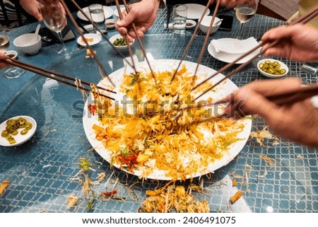 People mixing and tossing yusheng or yee sang during Chinese New Year dinner celebration. Slow shutter speed with motion blur intended.