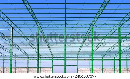 Metal roof beam and columns of new industrial factory building outline structure in construction area against blue sky background, symmetric view