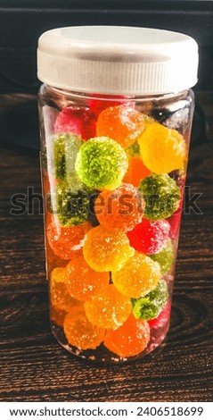 Colored round candy balls sprinkled with sugar a glass jar and on a wooden table.