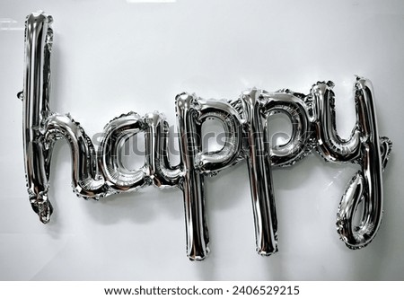 "The word 'happy' on the white wall, composed of silver balloons, signifies happiness."