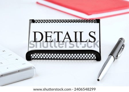 DETAILS the word on the business card standing on a stand next to a notepad, calculator and pen