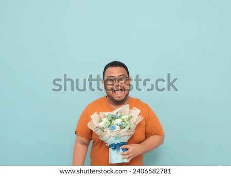 Asian men wearing glasses and brown clothes are carrying a bouquet of flowers while having a happy expression isolated on light blue background