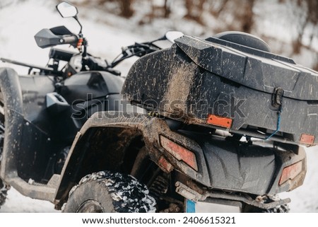  Close-up photograph, a quad rests on a snowy trail, showcasing the wintry adventure that awaits as it stands ready for an off-road journey through the frost-covered terrain