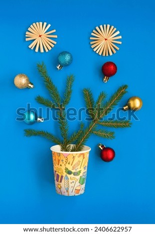 Christmas tree branches with Christmas toys in a paper cup with holiday pictures on a blue background, top view