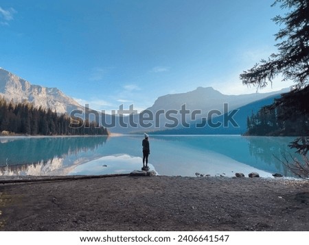 Person standing alone on rock on lake in early morning sun rays Canadian Rockies Royalty-Free Stock Photo #2406641547