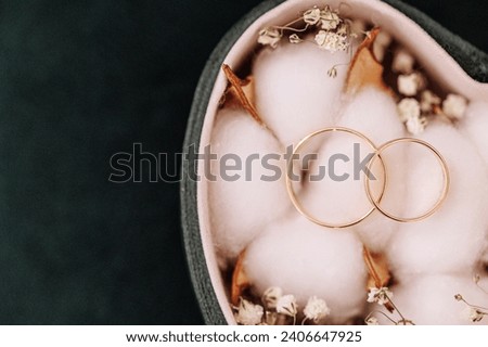 Two golden wedding rings rest on cotton balls in a heart-shaped box, surrounded by small dried flowers. Concept: Love, marriage, and the symbol of eternal union.