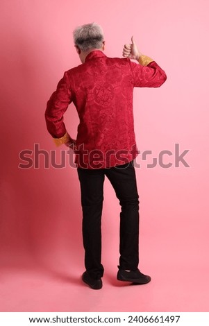 Happy Chinese new year. Asian Chinese energetic senior man wearing red traditional cheongsam qipao or changshan dress with gesture of  hands pointing isolated on pink background.