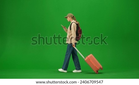 Portrait of person tourist isolated on chroma key green screen background. Young woman with suitcase walking and looking at the smartphone.