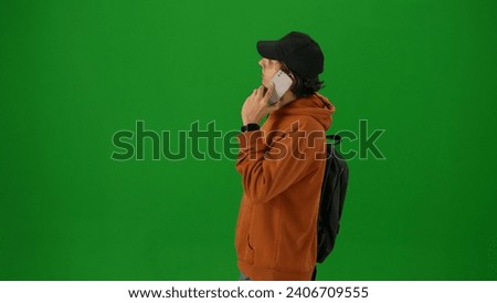 Portrait of person tourist isolated on chroma key green screen background. Close up shot young man talking on smartphone looking at the departure board.