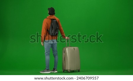 Portrait of person tourist isolated on chroma key green screen background. Young woman with suitcase standing and looking at the information flight board.