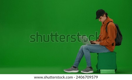 Portrait of person tourist isolated on chroma key green screen background. Young man sitting holding laptop and working, waiting for flight.