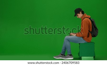 Portrait of person tourist isolated on chroma key green screen background. Young man sitting holding laptop and typing, waiting for flight.