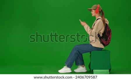 Portrait of person tourist isolated on chroma key green screen background. Young woman sitting holding smartphone listening music in headphones.