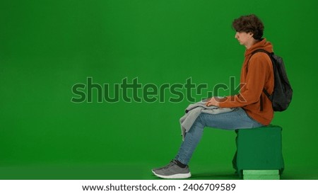 Portrait of person tourist isolated on chroma key green screen background. Young man sitting holding plaid ready to take nap waiting for flight.