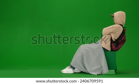 Portrait of person tourist isolated on chroma key green screen background. Young woman sitting covered in plaid with hood on, taking nap waiting for flight.