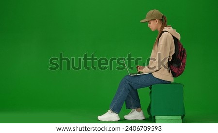 Portrait of person tourist isolated on chroma key green screen background. Young woman sitting holding laptop and typing, waiting for flight.