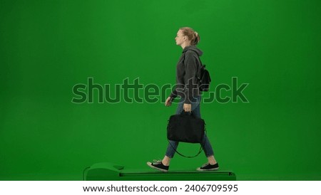 Portrait of person tourist isolated on chroma key green screen background. Young woman in casual clothing walking with laptop bag looking around.