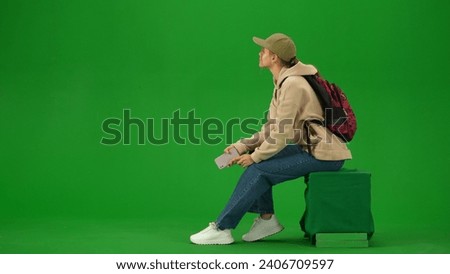 Portrait of person tourist isolated on chroma key green screen background. Young woman sitting holding smartphone looking at information board.