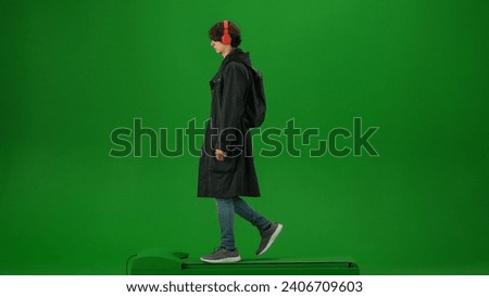 Portrait of person tourist isolated on chroma key green screen background. Young man in coat and headphones with backpack walking and listening music.