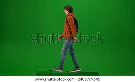 Portrait of person tourist isolated on chroma key green screen background. Young man in orange hoodie with backpack walking and looking around.