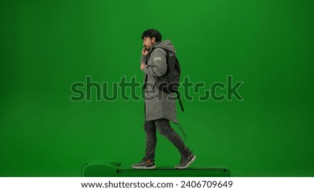 Portrait of person tourist isolated on chroma key green screen background. Adult man in winter coat with backpack walking and talking on smartphone.