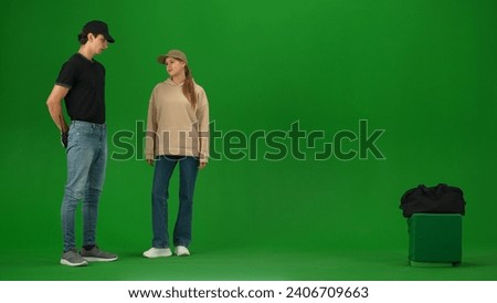 Portrait of person tourist isolated on chroma key green screen background. Young woman standing and looking at security man, black bag next to her.