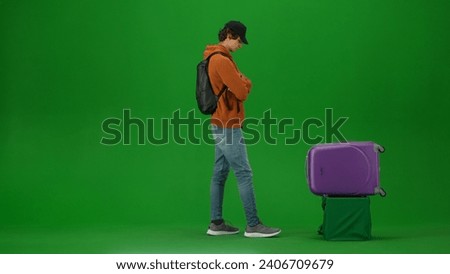 Portrait of person tourist isolated on chroma key green screen background. Young man standing waiting for his suitcase at the luggage carousel.