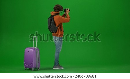 Portrait of person tourist isolated on chroma key green screen background. Young man with suitcase standing and taking pictures on his camera.