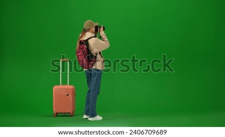 Portrait of person tourist isolated on chroma key green screen background. Young woman with suitcase standing and taking pictures on her camera.