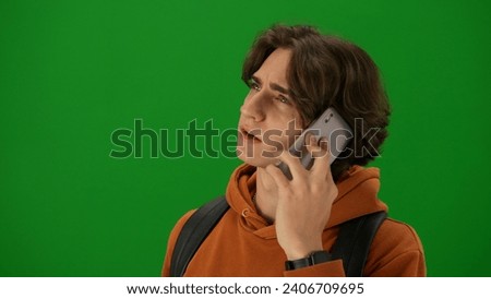 Portrait of person tourist isolated on chroma key green screen background. Close up shot young man talking on smartphone looking at the departure board.