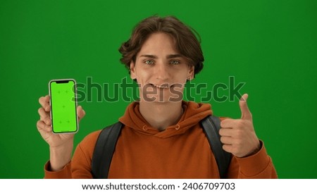 Portrait of person tourist isolated on chroma key green screen background. Close up shot young man holding smartphone with mockup smiling showing thumbs up.