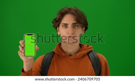 Portrait of person tourist isolated on chroma key green screen background. Close up shot young man holding smartphone with mockup smiling at the camera.