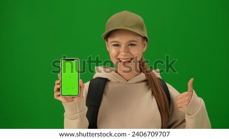 Portrait of person tourist isolated on chroma key green screen background. Close up shot young woman holding smartphone with mockup smiling showing thumbs up.