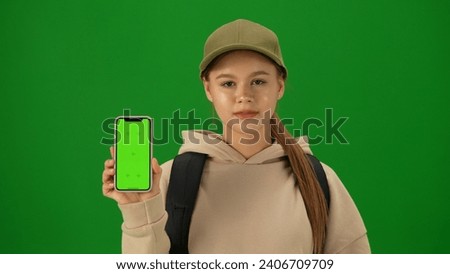 Portrait of person tourist isolated on chroma key green screen background. Close up shot young woman holding smartphone with mockup smiling at the camera.