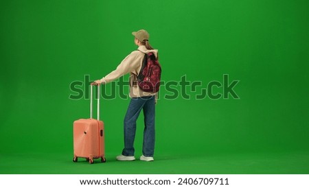 Portrait of person tourist isolated on chroma key green screen background. Young woman with suitcase standing and looking at the information board.